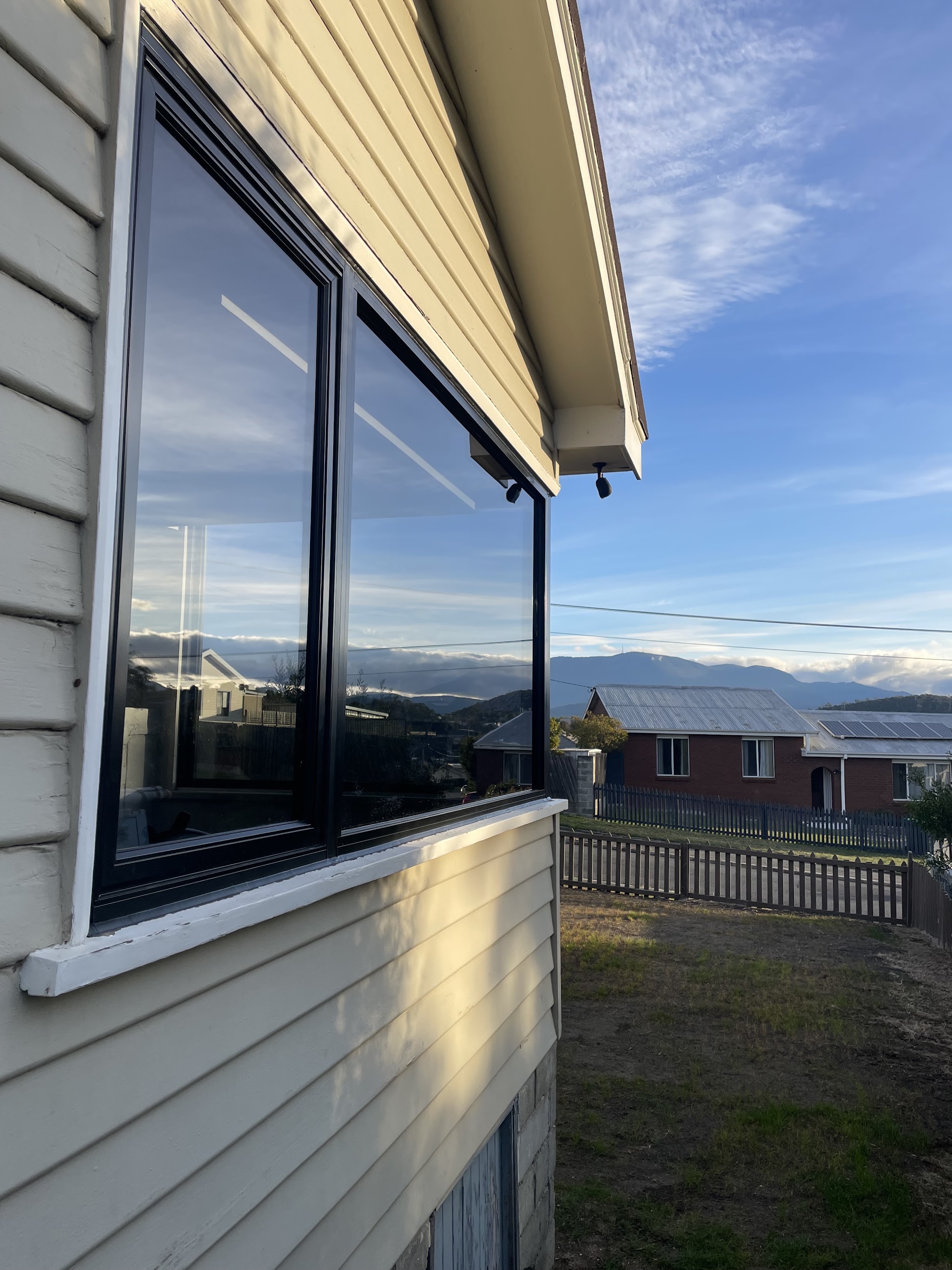 A finished black framed double glazed corner window on a cream weatherboard cottage