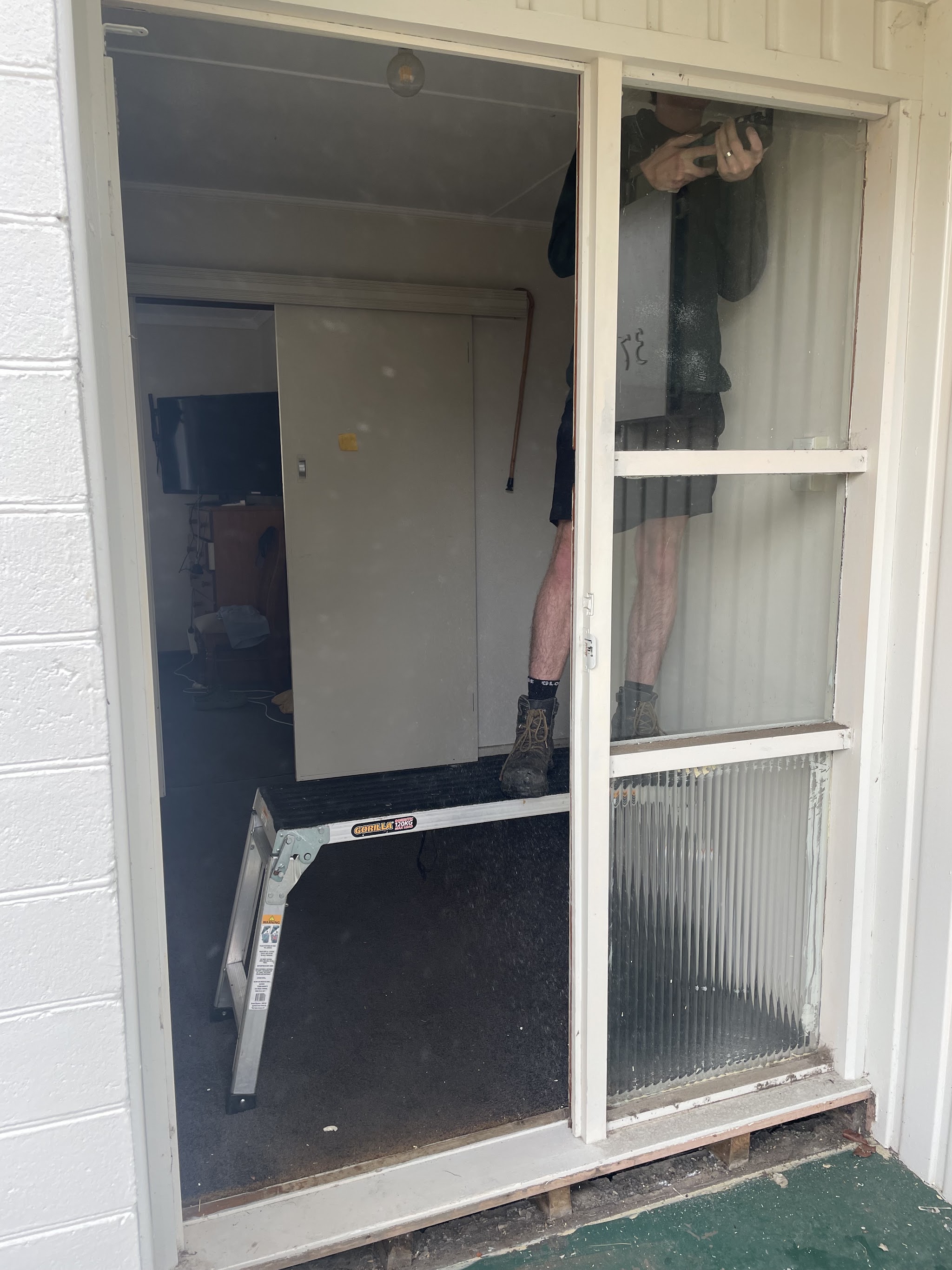 Taking out an old white timber framed door and sidelight on site, with the installer reflected in the remaining glass