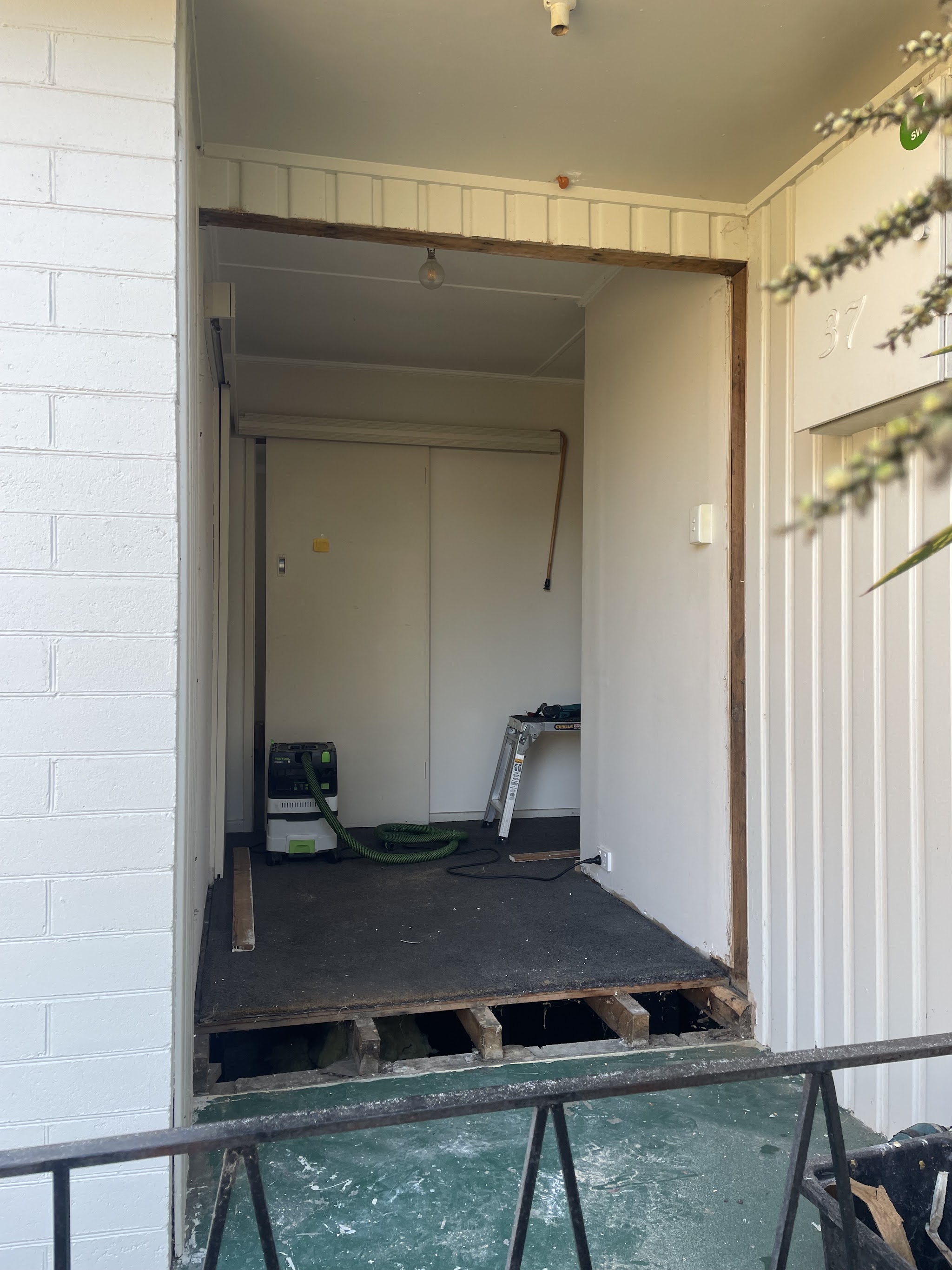 An entry opening stripped back mid job, with the removed glass panel resting on trestles outside