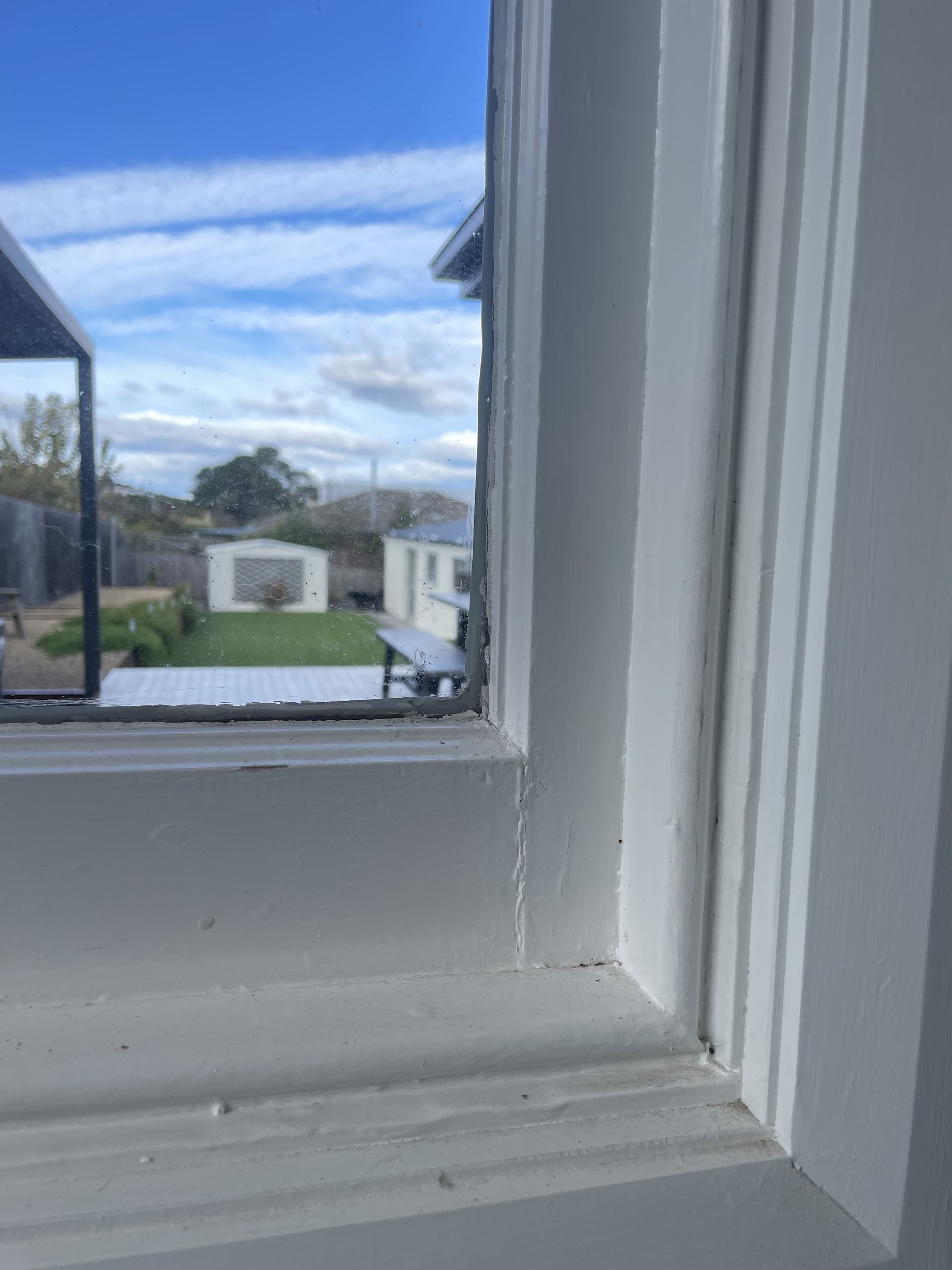 An old painted timber sash window with paint flaking off the sill and a visible gap at the frame