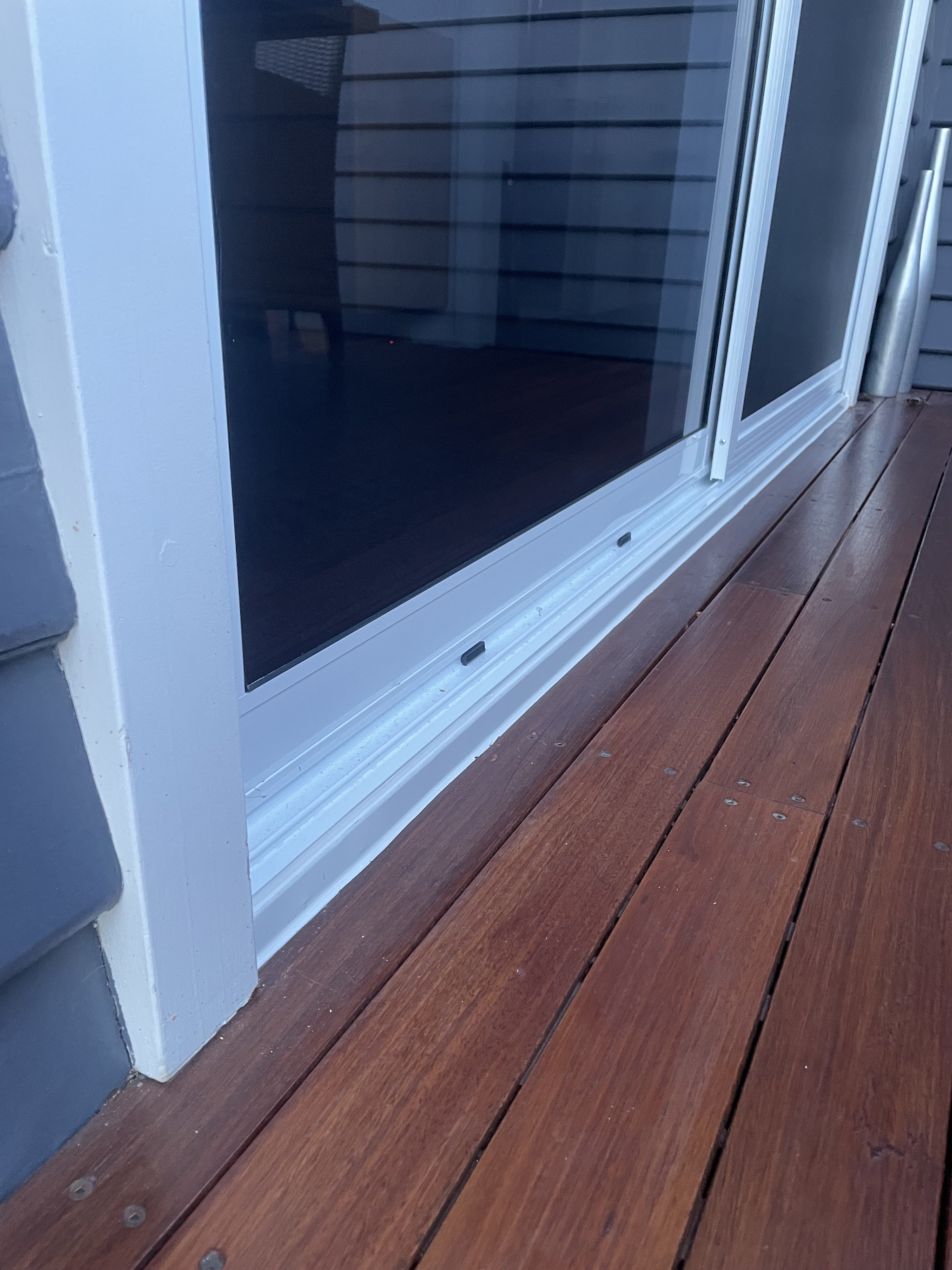 A finished white framed sliding door with tinted double glazing opening onto a merbau deck